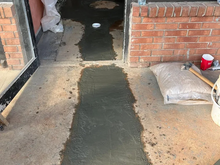 Fresh concrete patch poured over a plumbing trench at a doorway threshold
