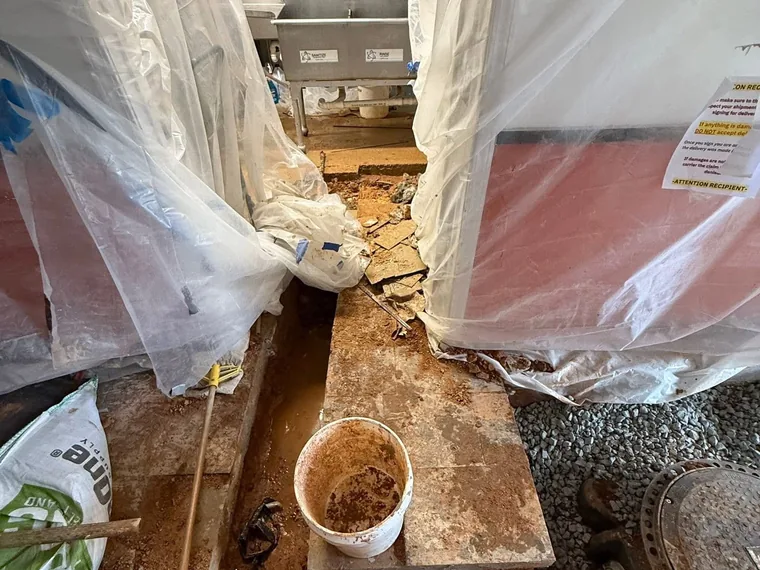 Tight back-of-house excavation near a three-compartment sink for grease trap plumbing