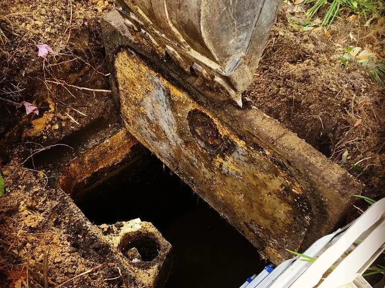 Excavator bucket lifting a heavy concrete septic tank lid