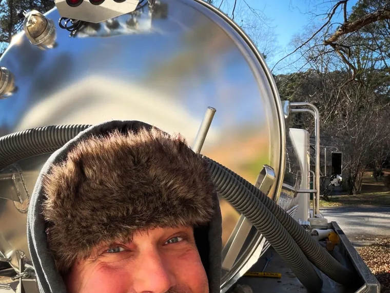 SepticRooter owner beside a stainless pump tanker in winter