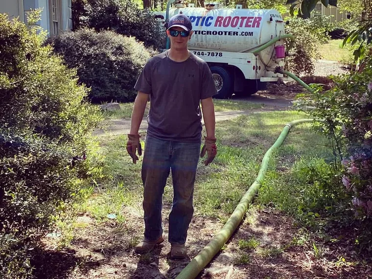 SepticRooter technician standing with pump hose run to septic tank