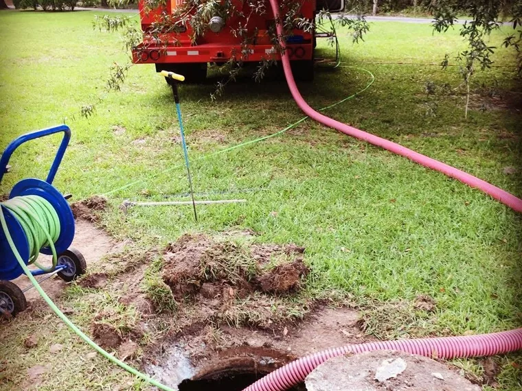 Red pump truck connected with hose running to open septic tank in yard